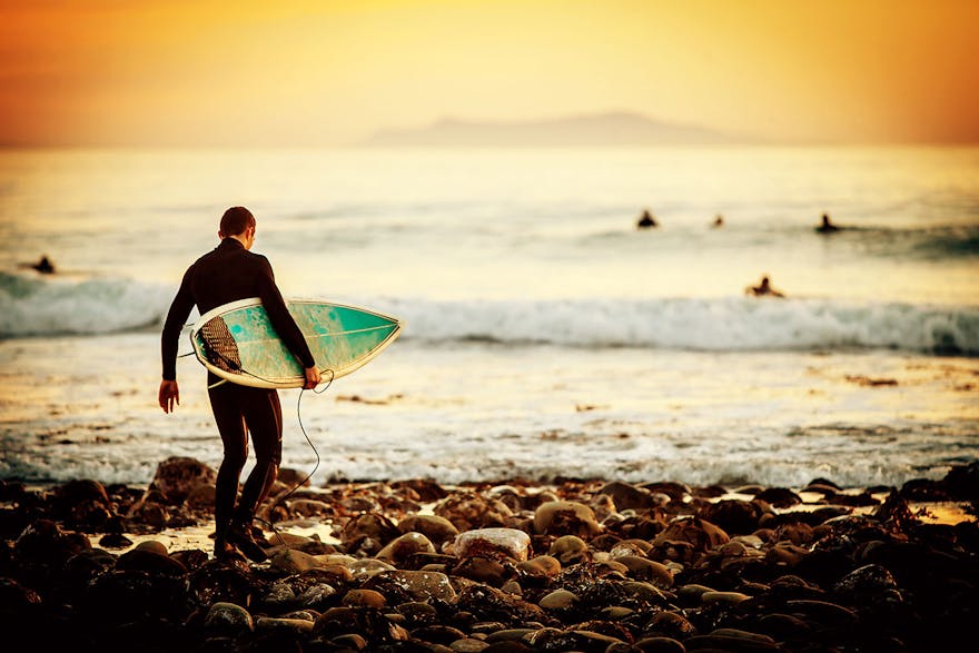 Surfer walking over rocks at sunset